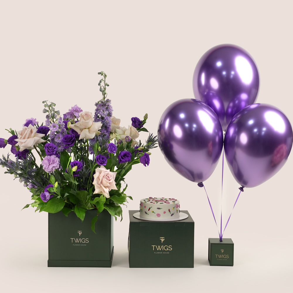 Subtle Bloom square flower box with quicksand roses and purple lisianthus, paired with a 1kg birthday cake and three purple chrome balloons in TWIGS beige or green packaging, available for same day flower delivery in Dubai when you buy flowers online.