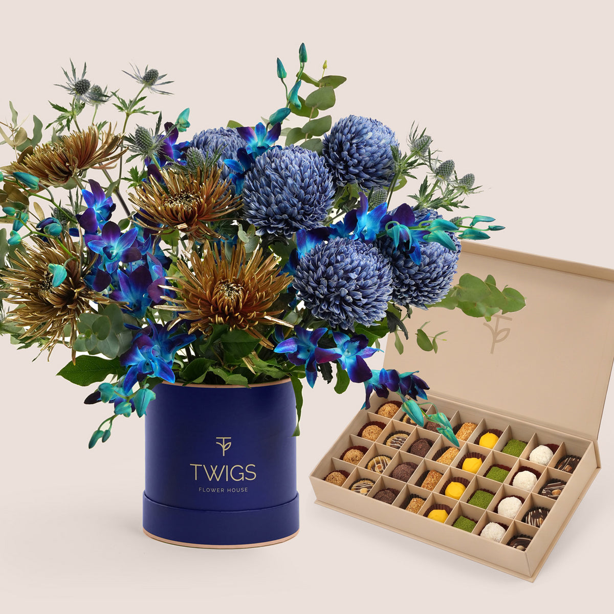 Navy TWIGS flower box with blue orchids and bronze chrysanthemums beside a box of truffles and petite fours, a Diwali flowers and sweets gift in Dubai