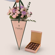 Violet Hues pink and purple rose bouquet in TWIGS cone-shaped bag next to open Bateel Rose Gold date chocolate box, gift bundle Dubai UAE
