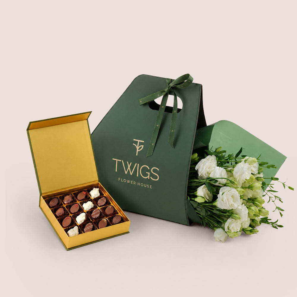 White lisianthus bouquet in TWIGS green gift bag next to open Bateel Palm date chocolate box, luxury gift bundle Dubai UAE