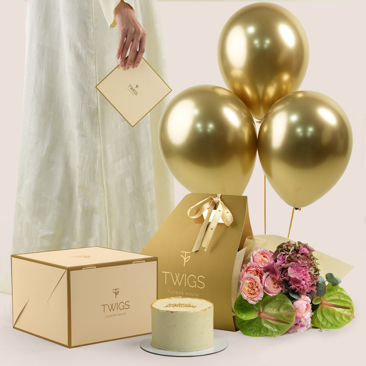 Isadora Celebration, flowers and cake and flowers gift set: a TWIGS Gold carry bag with pink roses, pink hydrangeas, and green anthurium leaves, paired with a 1kg cake and three gold chrome balloons.