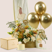 Aurelia Celebration, a luxury TWIGS Gold Garden box arrangement of white and peach roses, chrysanthemums, and gold anthurium leaves, paired with a 1kg cake and three gold chrome balloons.