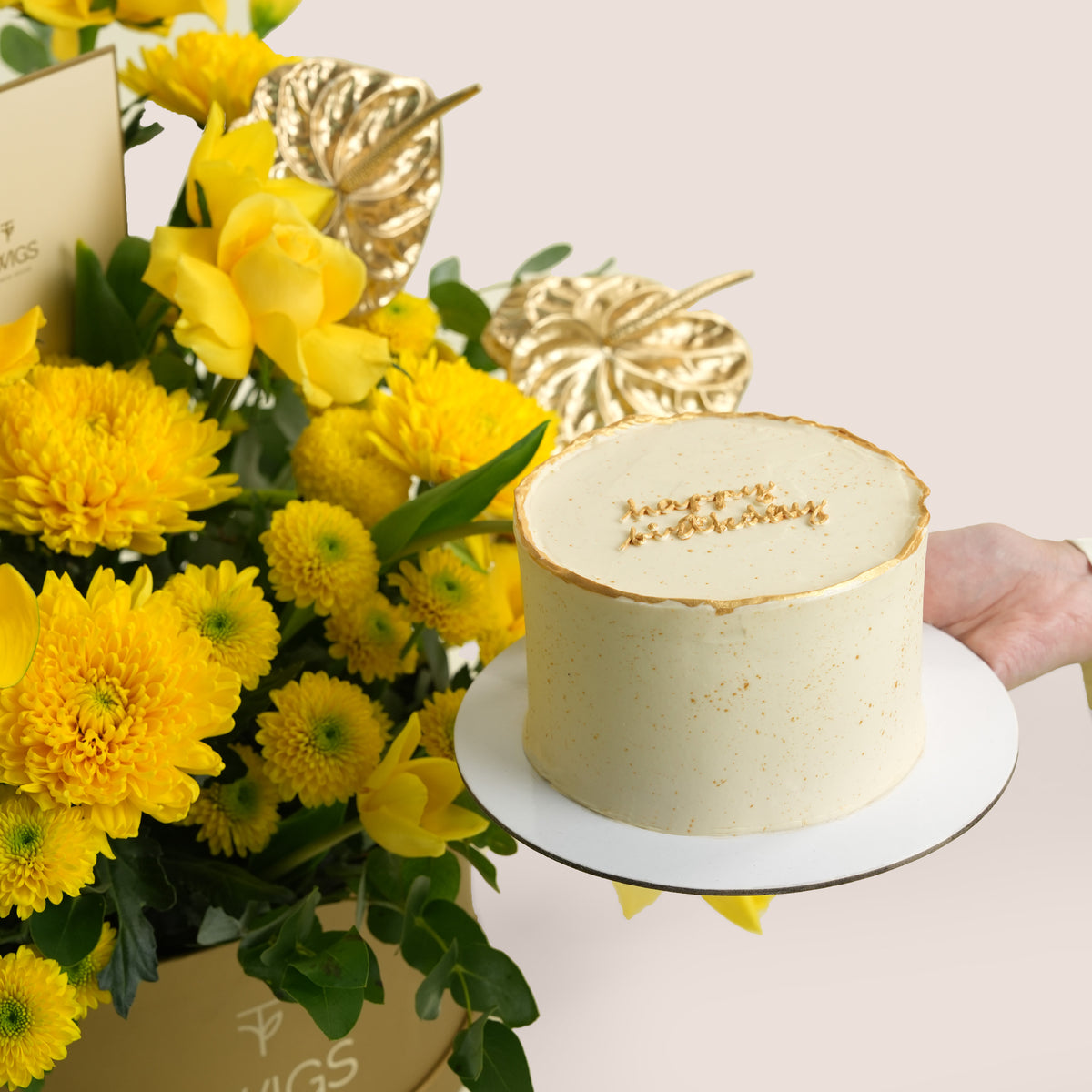 Solara Celebration, a vibrant yellow floral arrangement of calla lilies, chrysanthemums, roses, and gold anthurium leaves in a round TWIGS Gold box, paired with a 1kg cake and three gold chrome balloons.