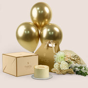 Lumina Celebration, flowers and cake with balloons gift set: a TWIGS Gold carry bag with white roses, peach spray roses, chrysanthemums, and a gold anthurium leaf accent, paired with a 1kg cake and three gold chrome balloons.