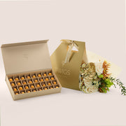 Aurelia Pairing, flowers and chocolate gift set: a TWIGS Gold gift bag with white roses, chamomiles, and a gold anthurium leaf accent, paired with a 32 piece premium bonbon box.