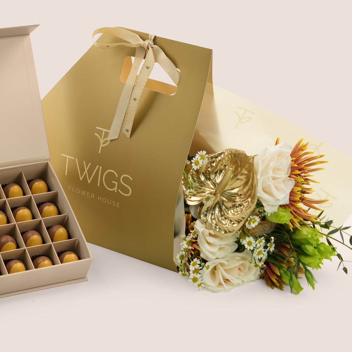 Aurelia Pairing, flowers and chocolate gift set: a TWIGS Gold gift bag with white roses, chamomiles, and a gold anthurium leaf accent, paired with a 32 piece premium bonbon box.