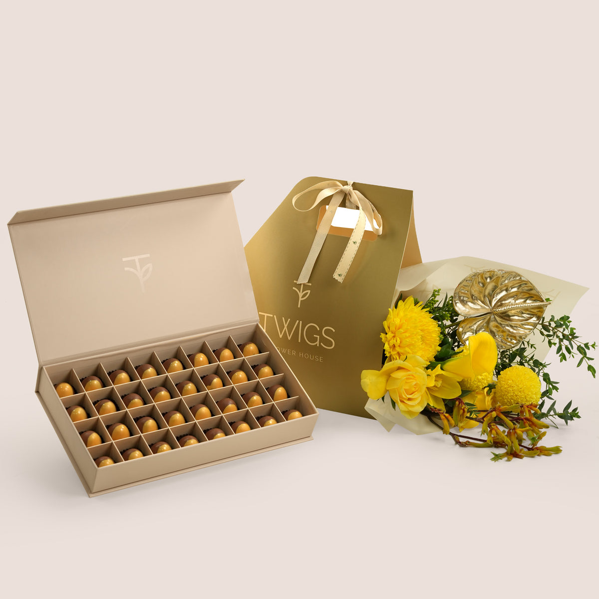 Solara Pairing, flowers and chocolate gift set: a TWIGS Gold carry bag with yellow roses, chrysanthemums, and a gold anthurium leaf accent, paired with a 32 piece premium bonbon box.