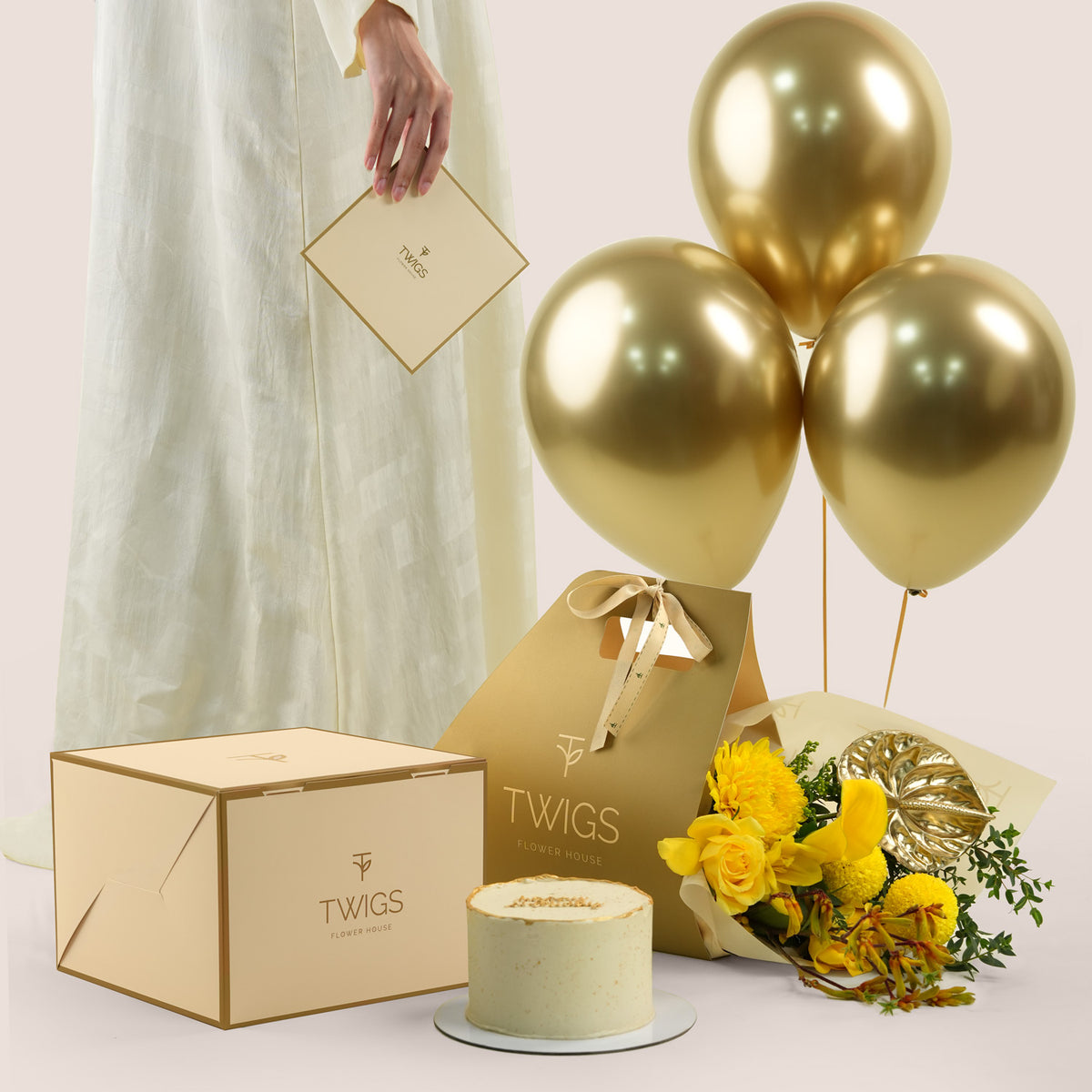 Solara Celebration, a TWIGS Gold carry bag with yellow roses, chrysanthemums, kangaroo paw, and a gold anthurium leaf accent, paired with a 1kg cake and three gold chrome balloons.