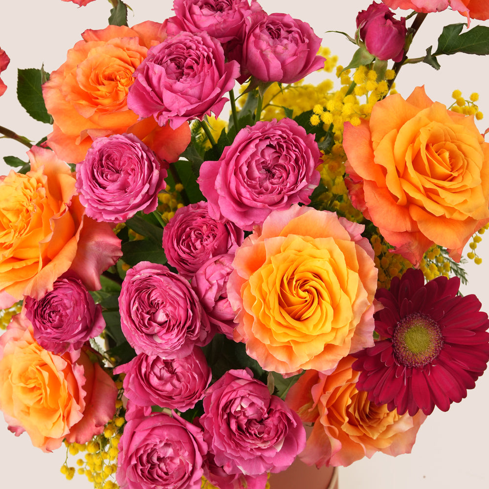 Bouquet of pink, orange, and yellow flowers with a red flower in the foreground on a light background.