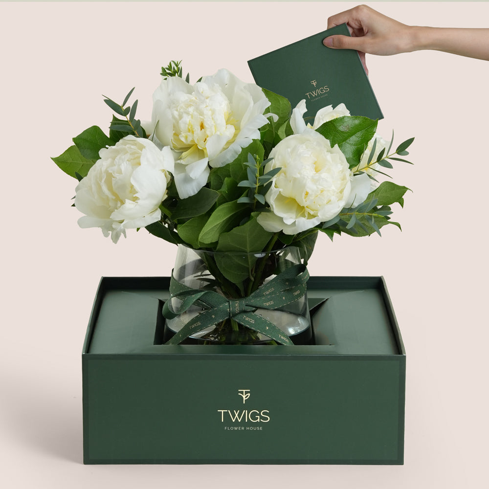 White peonies arranged in a glass vase with TWIGS signature carry flower box in beige and green packaging