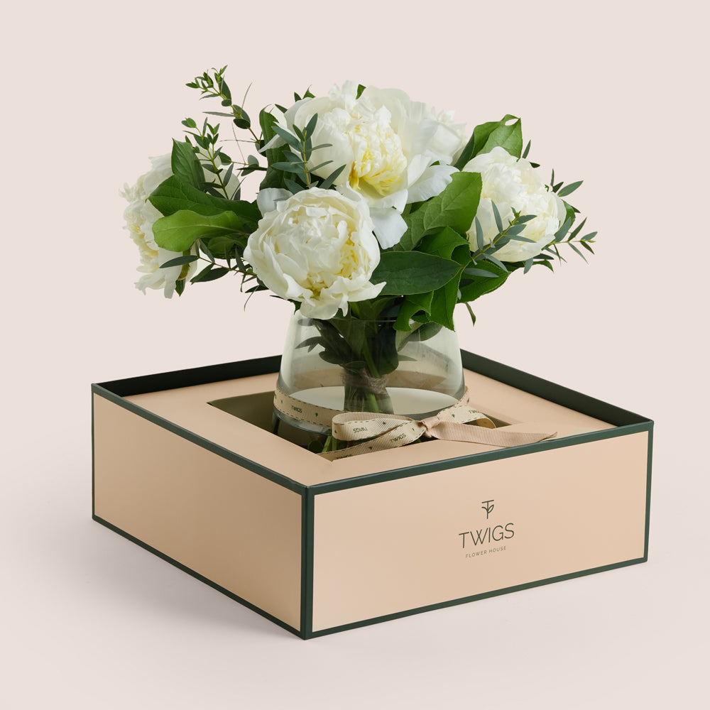 White peonies arranged in a glass vase with TWIGS signature carry flower box in beige and green packaging