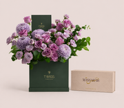 Purple roses and lilac chrysanthemums in a tall green TWIGS box beside a Massarah Her perfume oil set, TWIGS x Light of Sakina collaboration