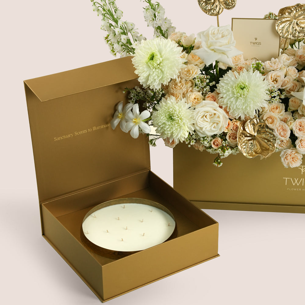 Lumina, a luxury TWIGS Gold Garden box arrangement of garden roses, chrysanthemums, and gold anthurium leaves, paired with the Palace Candle by Light of Sakina and six gold chrome balloons.
