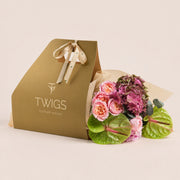 Isadora, a TWIGS Gold carry bag with garden roses, pink hydrangeas, and green anthurium leaves, on a light beige background.