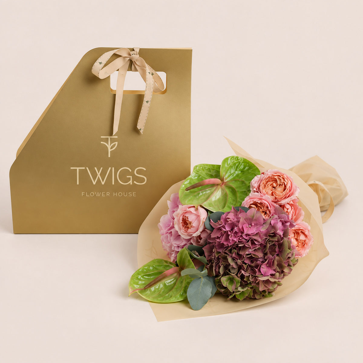 Isadora, a TWIGS Gold carry bag with garden roses, pink hydrangeas, and green anthurium leaves, on a light beige background.