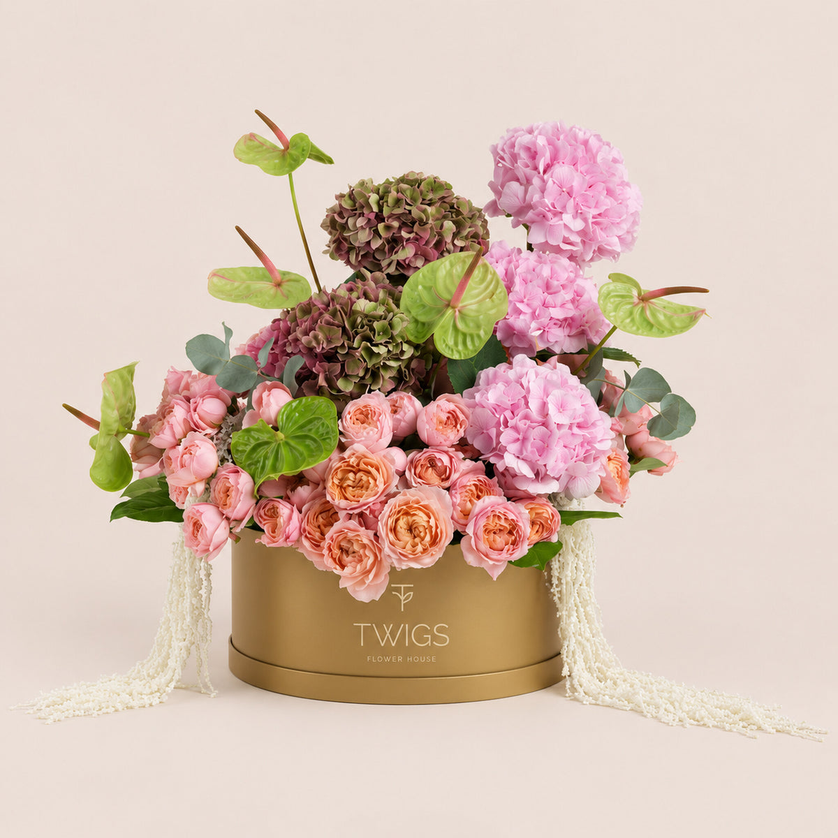 Isadora, a romantic floral arrangement of pink hydrangeas, two toned hydrangeas, Juliet garden roses, and green anthurium leaves in a round TWIGS Gold box.